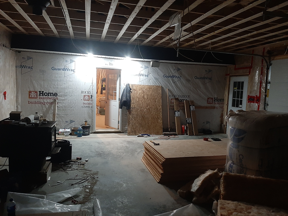 Dimly lit storage area with insulation and stacked plywood on the floor.