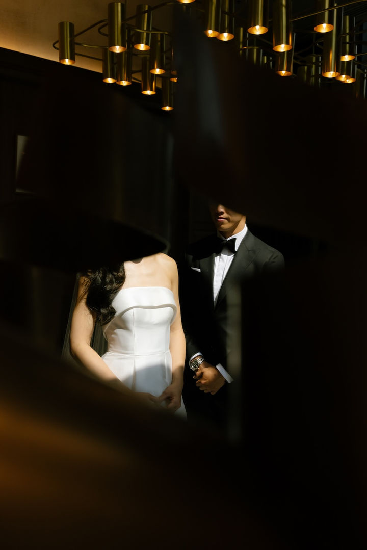 Bride and groom standing together in dramatic light, partially obscured by shadows.