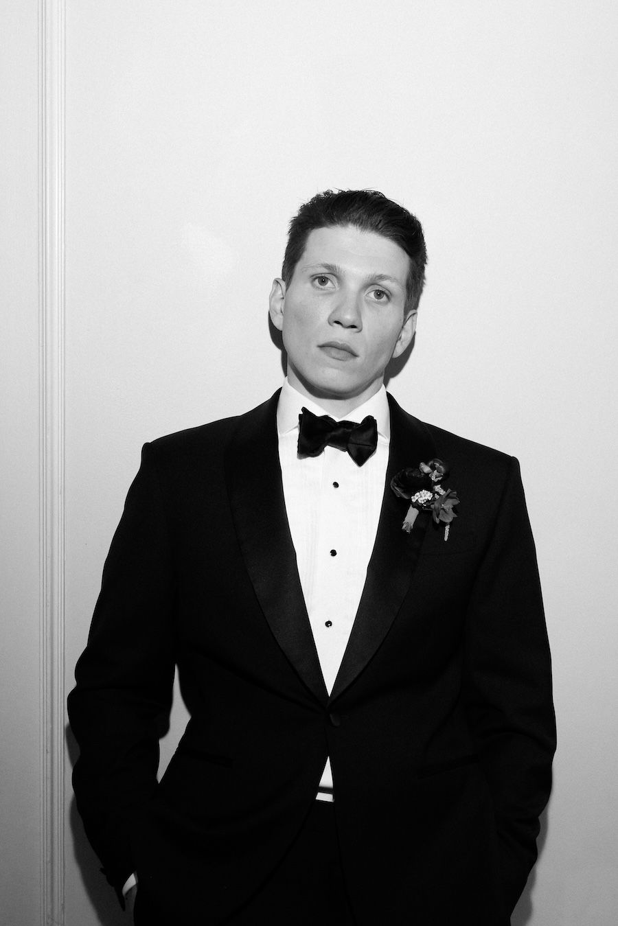Groom in black tuxedo with bow tie and boutonniere, looking forward for a portrait shot