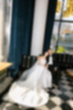 Bride in white gown, groom in tuxedo, seated on dark couch