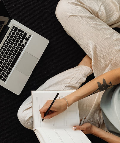 Dame som skriver i bok foran laptop