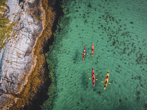 Kayakers paddling through Arctic waters on Hinnøya surrounded by fjords, mountains and coastal scenery in Northern Norway.