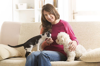 Mulher sentada no sofá alimentando gato no colo e abraçando cão com a outra mão