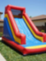 Large red, blue, and yellow inflatable slide on grass.