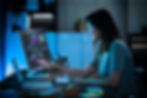 A lady in a dark room working in front of a computer showing a dark-mode report on the screen