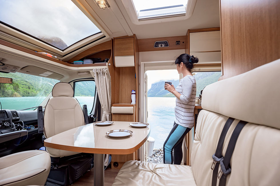 Eine Frau steht, mit einem Kaffeebecher in der Hand, in einem Wohnmobil. Ihr Blick ist an der offenen Wohnmobiltür nach draußen gerichtet.