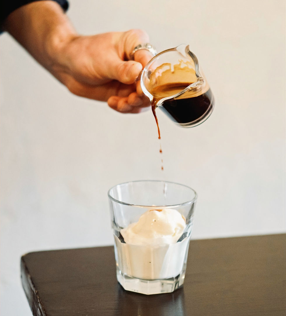 ręka wylewa kawę espresso ze szklanego dzbanuszka na lody w szklance stojącej na stole