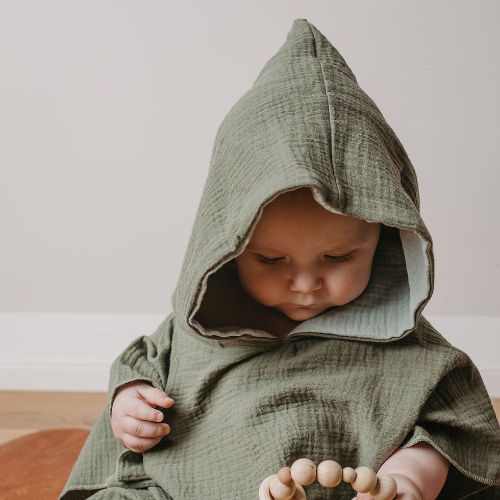 Miniaturbild: Kleinkind sitzt am Holzboden und hat einen Badeponcho aus Musselin aus Biobaumwolle von Mafee an