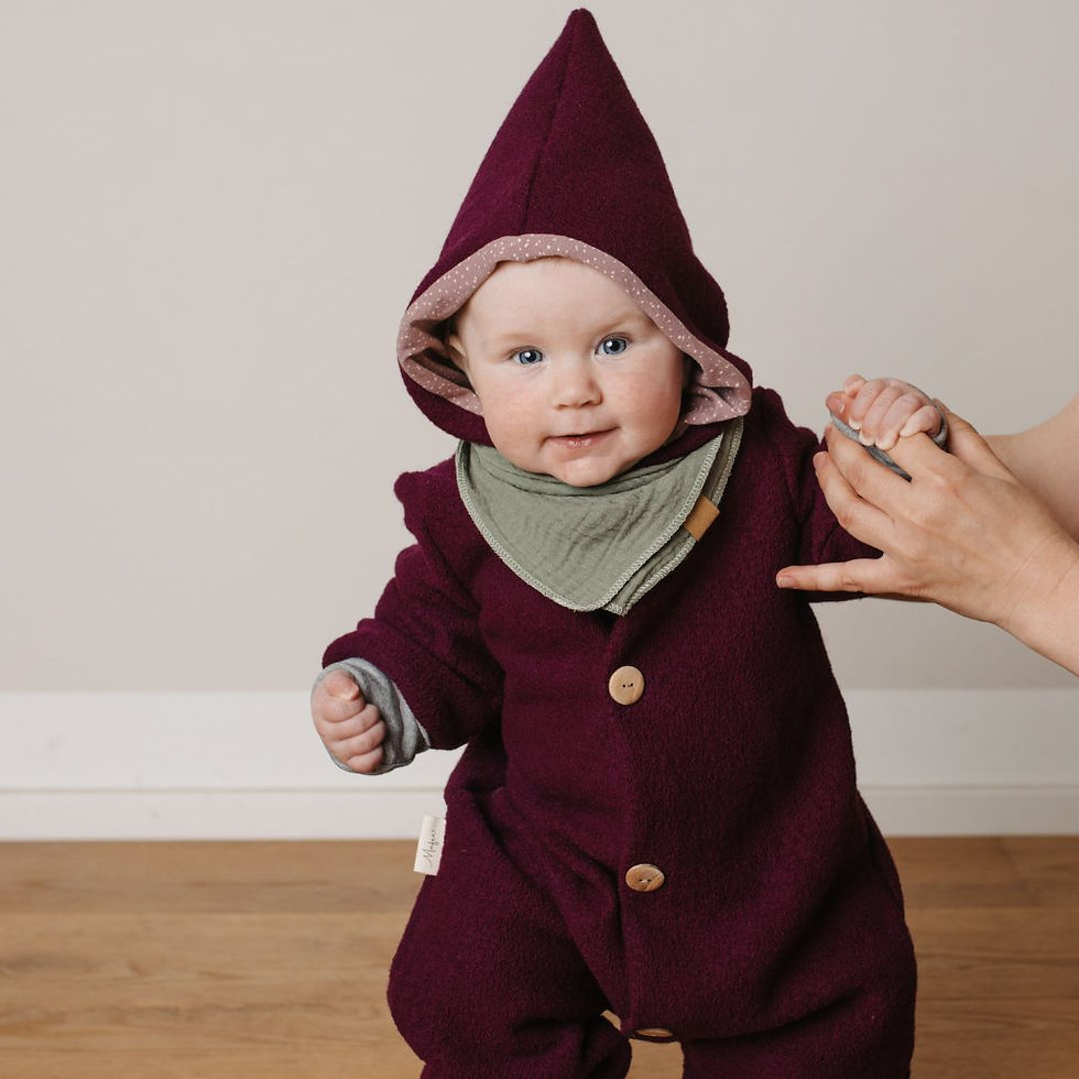 Baby sitzt am Boden mit Wollwalkanzug in rosa aus Merinowolle mitwachsend von Mafee spielt dabei mit Lederpatscherl