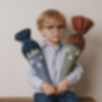 Ein kleiner Junge mit Brille und hellblauem Hemd hält stolz zwei Schultüten im Arm eine blaue und eine grüne,