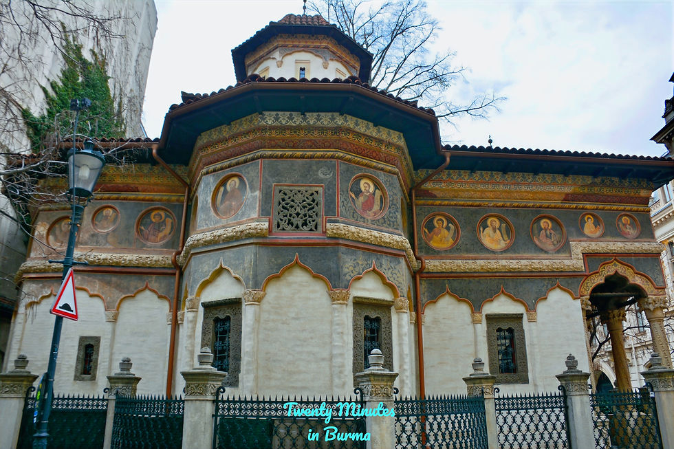 Ornate church facade with religious frescoes, arch designs, and a black wrought iron fence. A streetlamp and bare tree in the background. The Church of the "Stavropoleos" Monastery, Old Town, Bucharest, Romania
