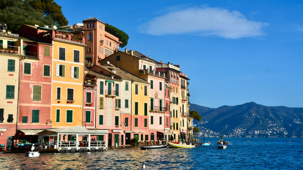 Portofino, Italy's shoreline with pastel colored buildings and small boats along the shore.