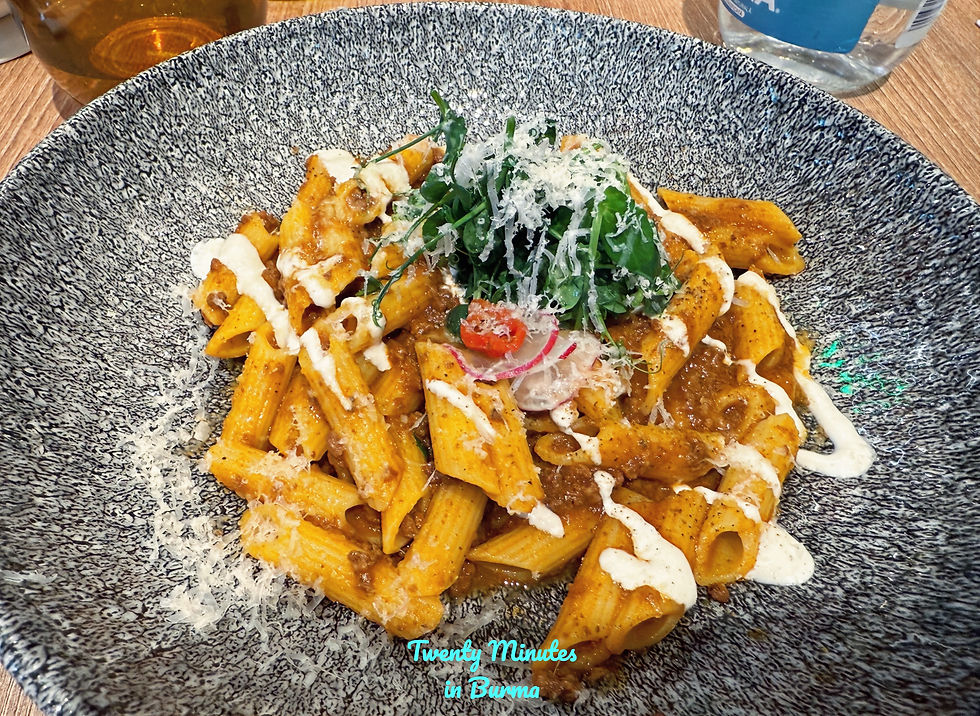 Penne pasta with sauce, garnished with greens and radish, drizzled with cream on a textured plate. Wooden table with orange glassware. AveForchetta, Bucharest, Romania