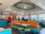 Diner scene with people ordering at a counter and seated in booths. Bright colors, a sign reading "Queen," and a mural outside. Casual mood. Island Queen, Vashon Island, Washington.