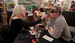 A couple participating in a blindfolded tasting at a restaurant table, illustrating a sex therapy dinner event designed to normalize intimacy conversations.