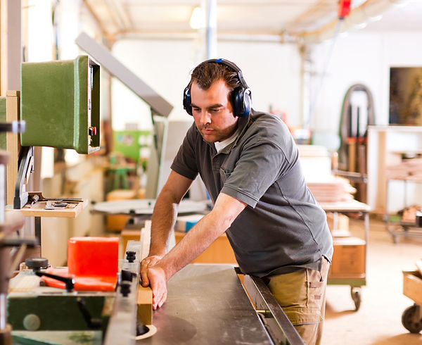 Man with earmuffs sawing wood in workshop