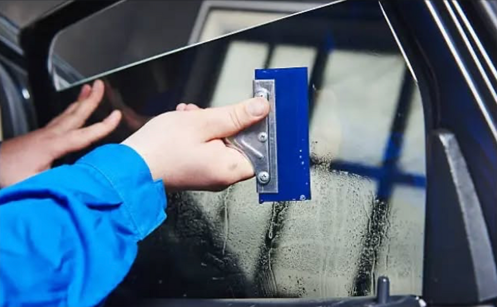 Technician smoothing window tint film on vehicle glass