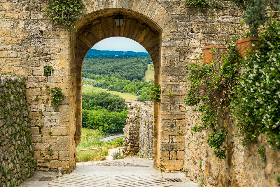Medieval Archway in Stone Brick Wall with Cobblestone Road Looking Out into Countryside.jp