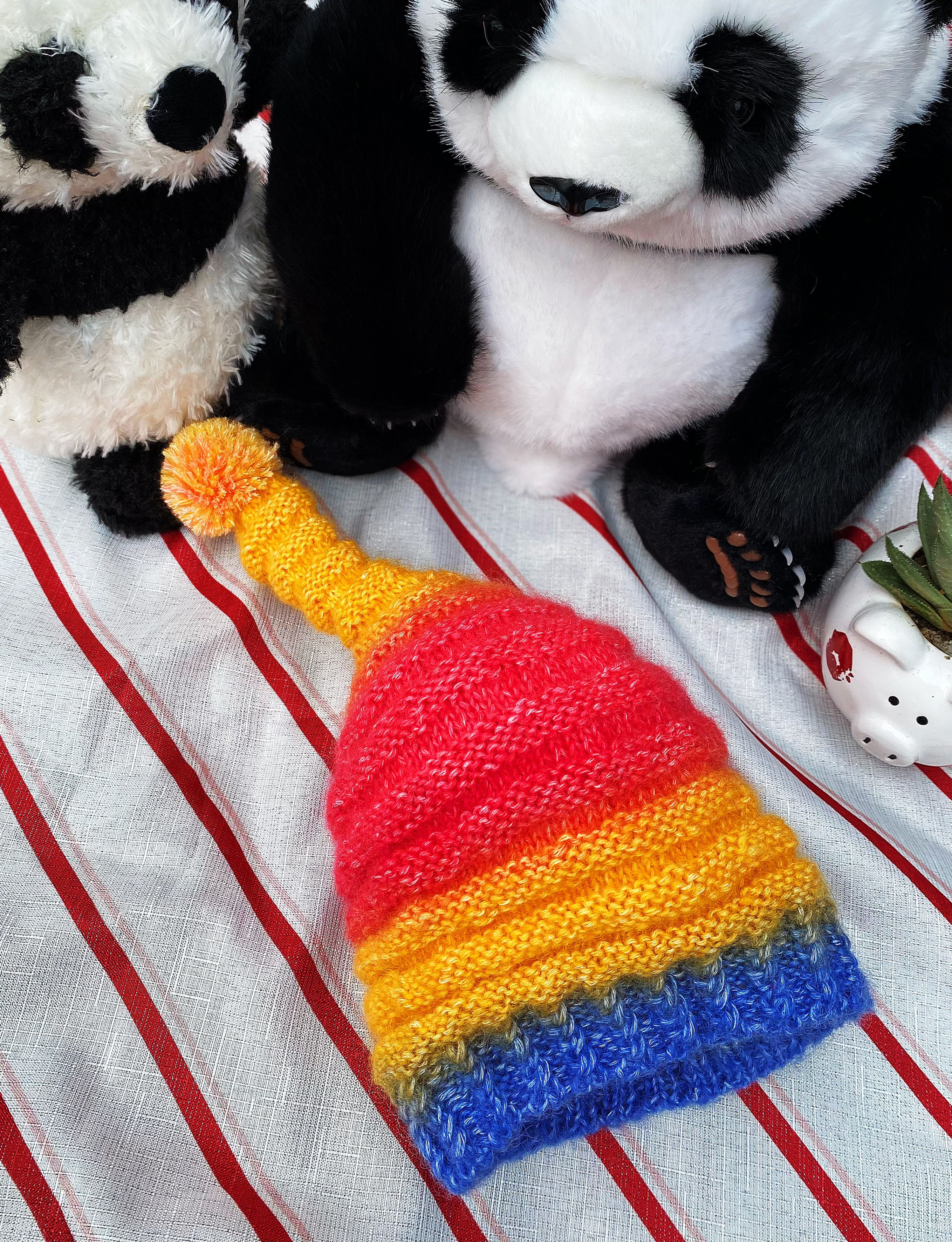 Our adorable handmade hat features a vibrant blend of red, orange, and blue, topped with a cheerful pom-pom