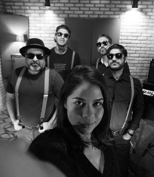 Foto dos integrantes da banda Bug do Milênio, na cor preto e branco, onde no centro está a vocalista Mylena segundo a câmera, e os demais integrantes, 4 rapazes, ao redor dela.