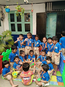 Junior KG classmates in blue uniforms playing together in the school's fenced outdoor area.