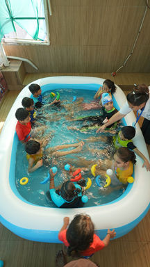 A group of preschoolers and teachers enjoying a water play activity in an inflatable pool inside the classroom.