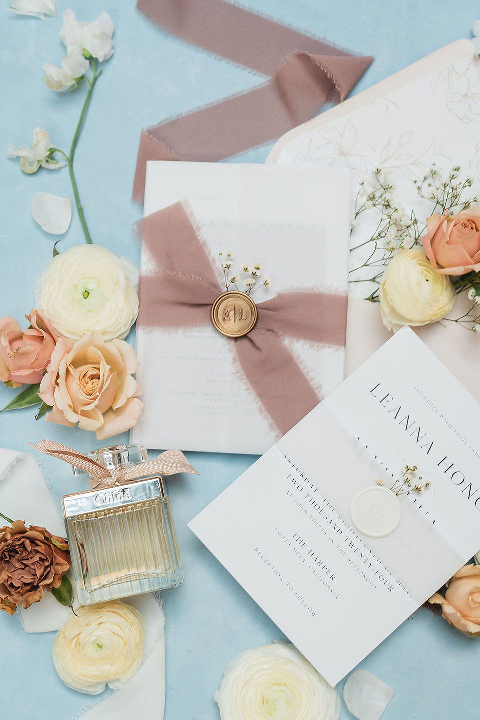 Wedding invitation details with perfume and flowers in a flat lay close up shot by Alvis Pham Photography, Orange County California Wedding Photographer