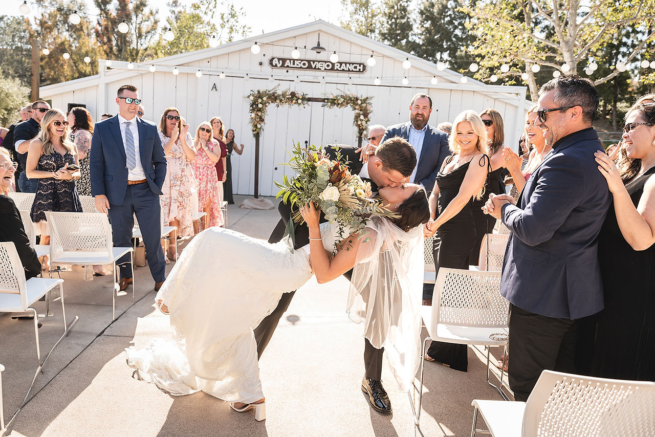 Bride and groom dip and kiss during the exit at the outdoor ceremony at The Barn at Aliso Viejo Ranch by Paper Birch Collective, California Wedding Photographer in Orange County