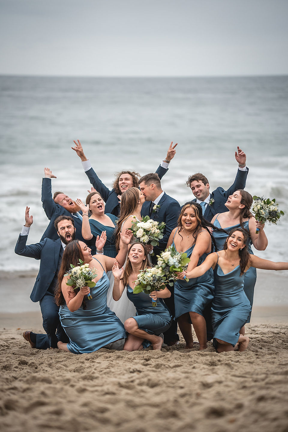 Wedding party cheers as newly weds kiss for Beach photoshoot for a Wedding at Occasions at Laguna Village in Laguna Beach photo by Paper Birch Collective, California Wedding Photographer in Orange County