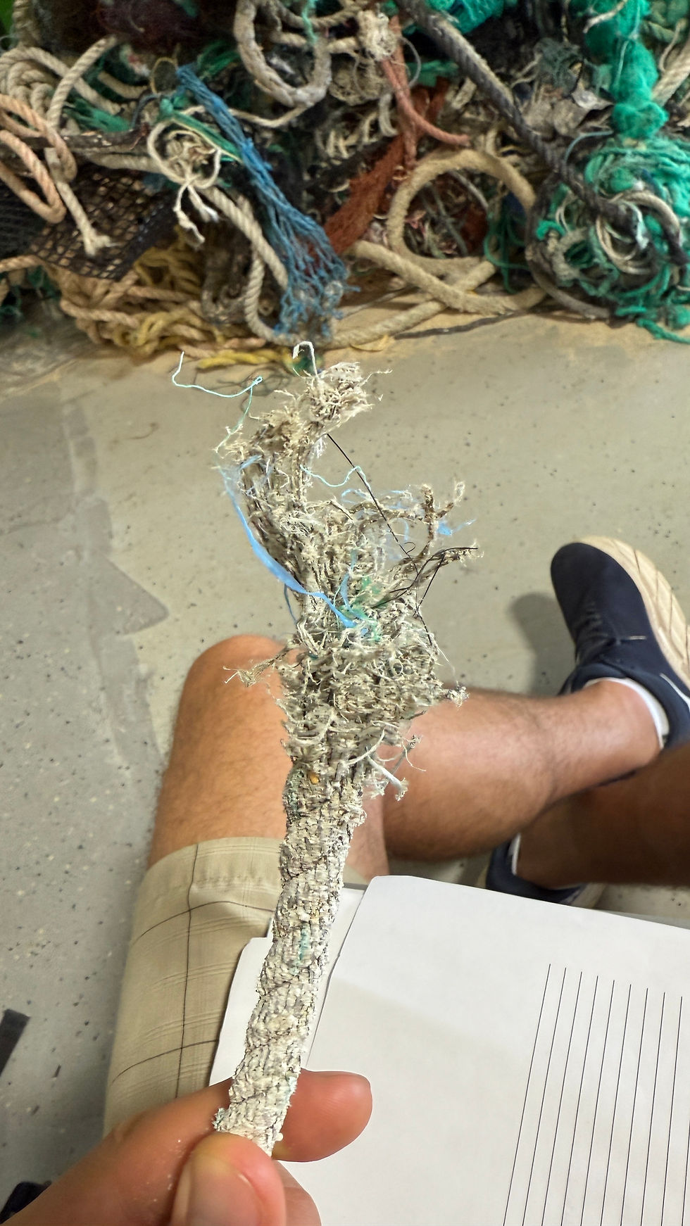 Holding a piece of plastic Derelict Fishing Gear collected by CMDR with a conglomerate in the background.