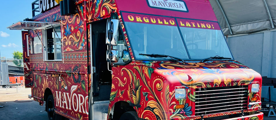 Mayorga Coffee 14‑ft custom food truck – a vibrant Latin‑inspired mobile espresso bar built by United Food Truck, featuring a red‑orange “Orgullo Latino!” wrap, rooftop illuminated “COFFEE” sign, exterior speaker & 50 W LED floodlight, service window, rear mesh door with ladder, generator caging, detailed floor‑plan blueprint, high‑end coffee equipment, refrigeration & display cases, stainless‑steel workstations, and safety systems, photographed in Rockville, MD.