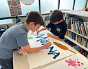 Two teen boys painting a sign