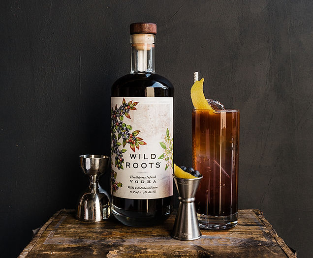 Huckleberry vodka bottle with jigger full of small fruit and a glass with lemon garnish.