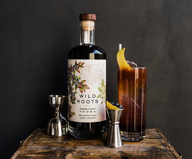 Huckleberry vodka bottle with jigger full of small fruit and a glass with lemon garnish.
