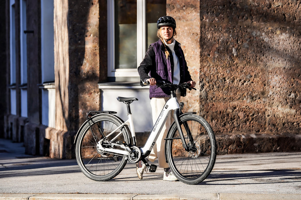 Frau mit weißem SIMPLON E-Bike vor Hauswand