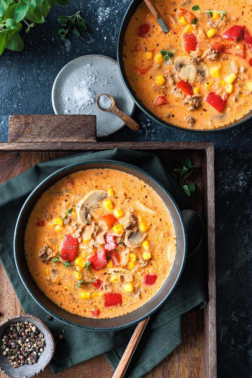 Foodfotografie einer in dunklen Schalen geschmackvoll und professionell angerichteten Pizzasuppe mit Champignons, Paprika und Mais