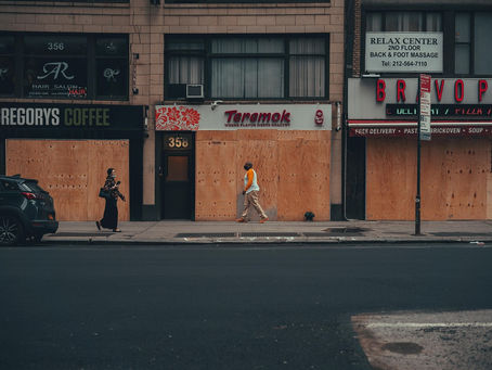 Je ziet hier een winkelstraat waarvan alle winkels gesloten zijn met houten planken voor de deuren.