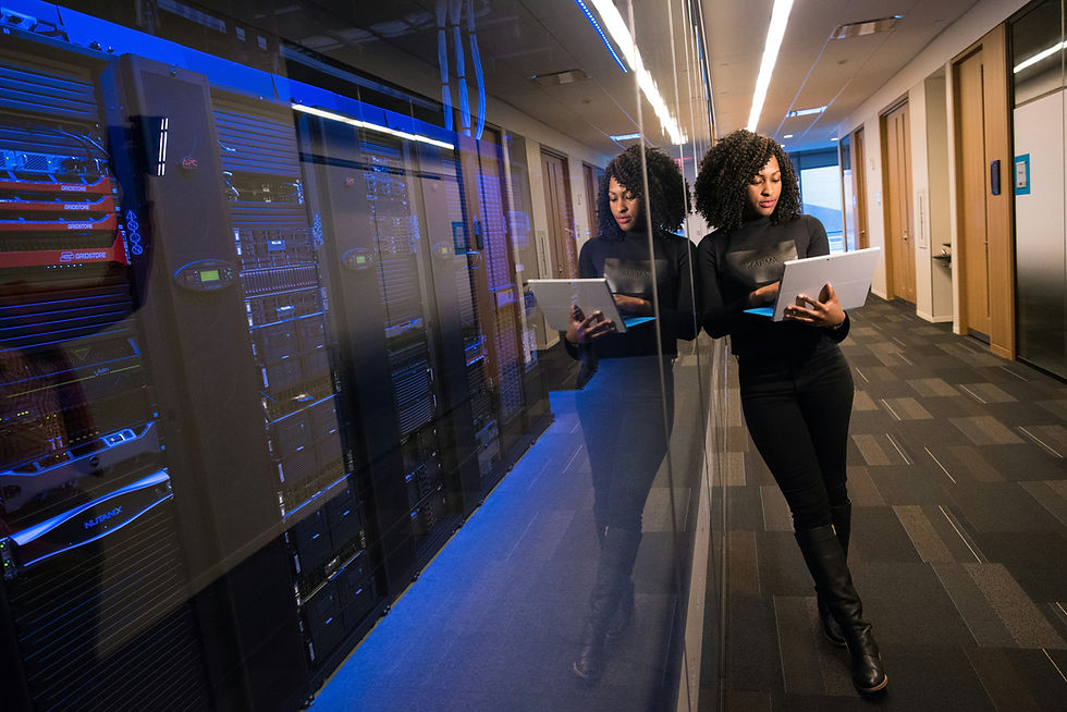 Black women leaning against the window of a server room holding a laptop.