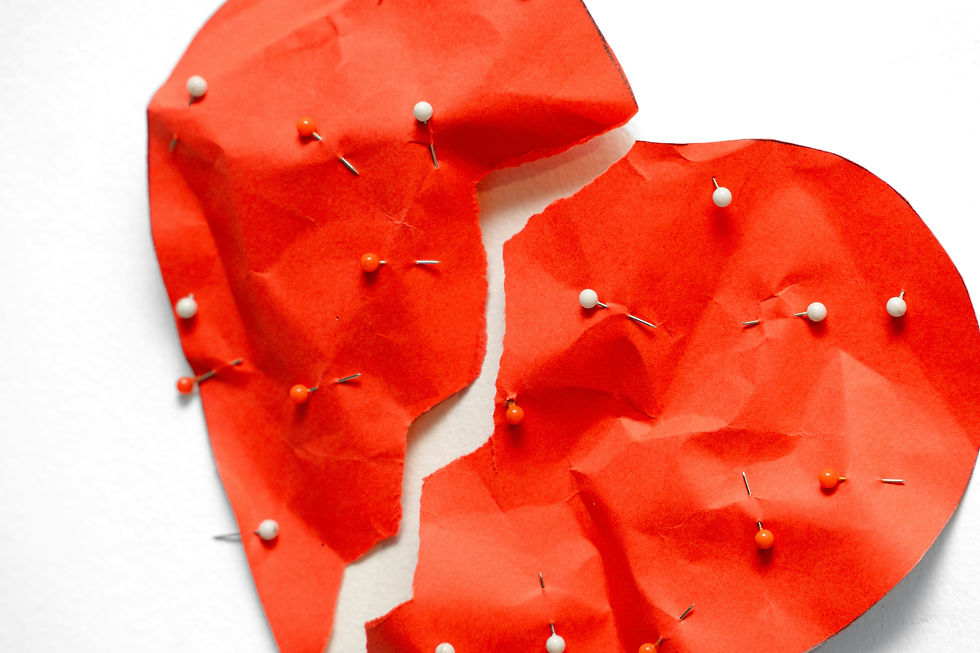 A torn red paper heart with white and orange pins on a white background, symbolizing heartbreak or emotional pain.