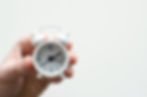 Hand holding a small white alarm clock showing 3:55. Plain white background, suggesting simplicity and focus on time.