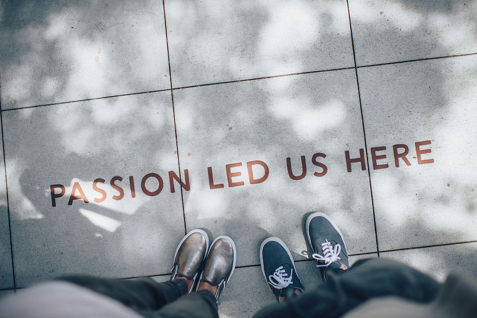 Two people stand on a sunlit sidewalk with text "PASSION LED US HERE" on the tiles. Shadows of leaves add a calm, reflective mood.