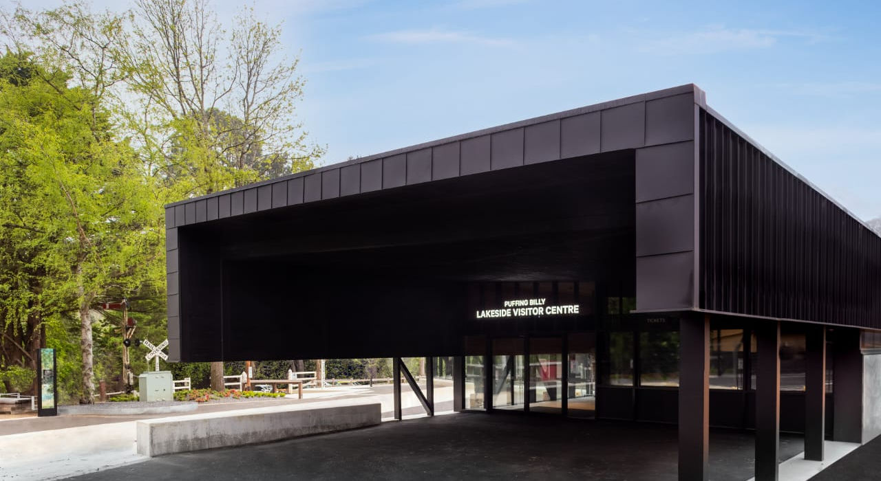 “Contemporary black building near train tracks under clear blue sky.”
