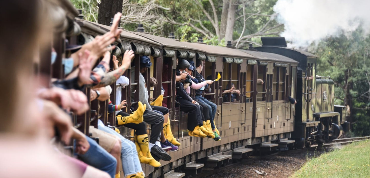 “Passengers riding open carriage steam train through mountain forest.”