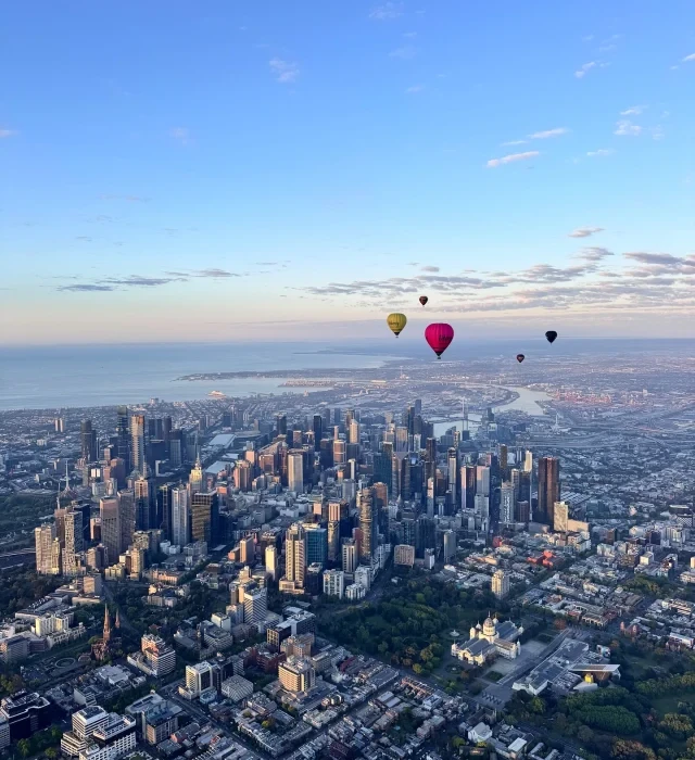 Series of hot air balloons drifting across the horizon under clear blue sky.