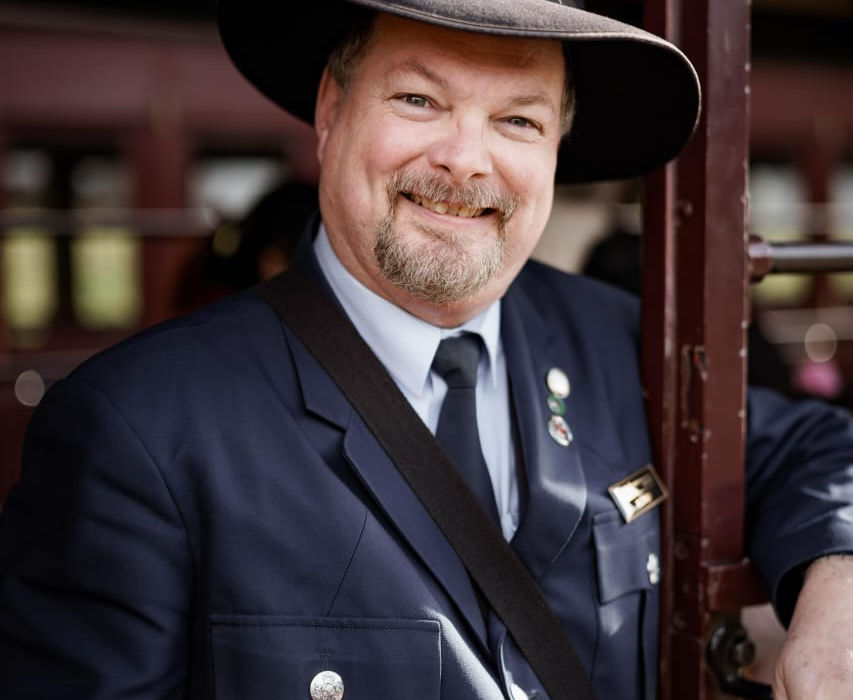 “Train conductor greeting passengers with a friendly smile.”