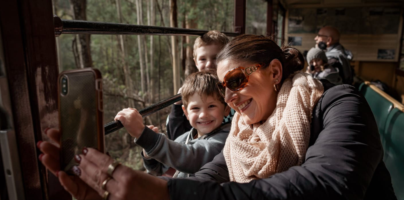 “Tourists taking selfies while riding an open-air steam train.”