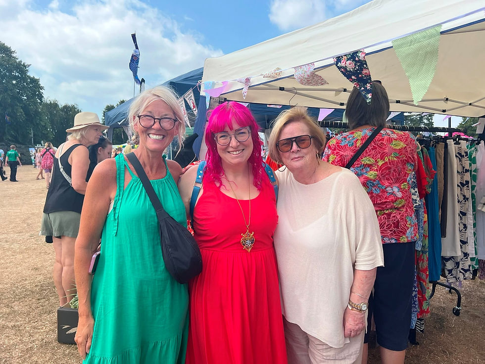 Three adults smiling at an outdoor community carnival, colorful clothes and bunting, landscape photo