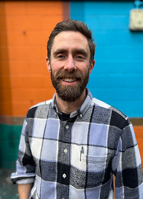 Smiling image of white man in 40's with a checked shirt and beard against a blue and orange background