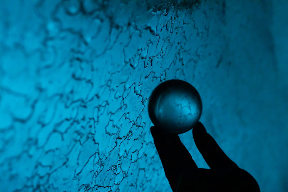 Silhouette of a hand holds a glass sphere against a textured, blue-lit wall. The scene has a mysterious and serene ambiance.