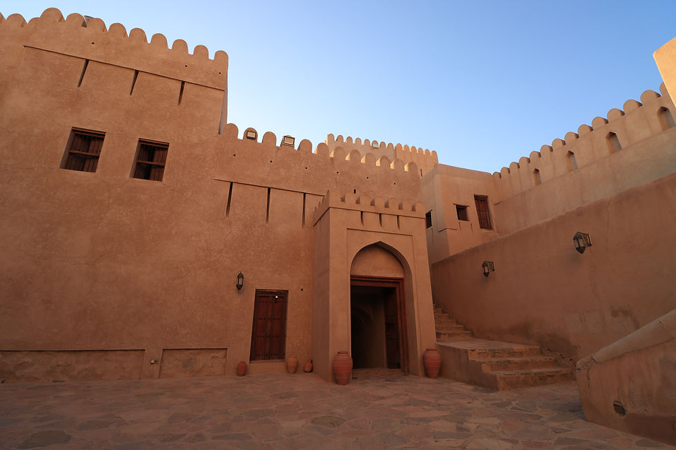 Ancient desert fortress with brown adobe walls, arched door, clay pots, and steps. Clear blue sky background evokes tranquility.